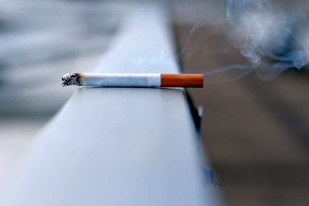 A lit cigarette sitting on a ledge outside.