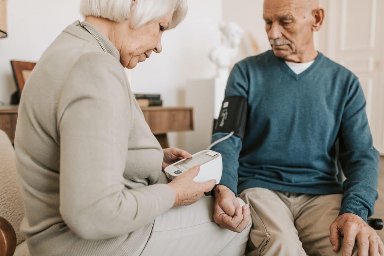 Wife helping her husband take his blood pressure with an at home monitor.