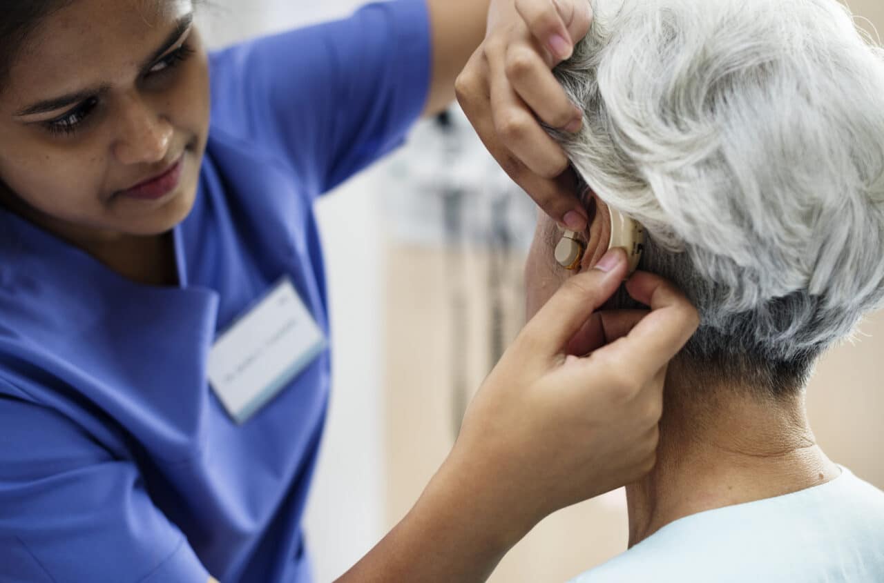 A medical provider fitting an elderly woman with a hearing aid.