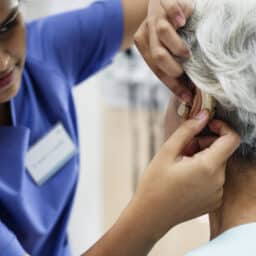 A medical provider fitting an elderly woman with a hearing aid.