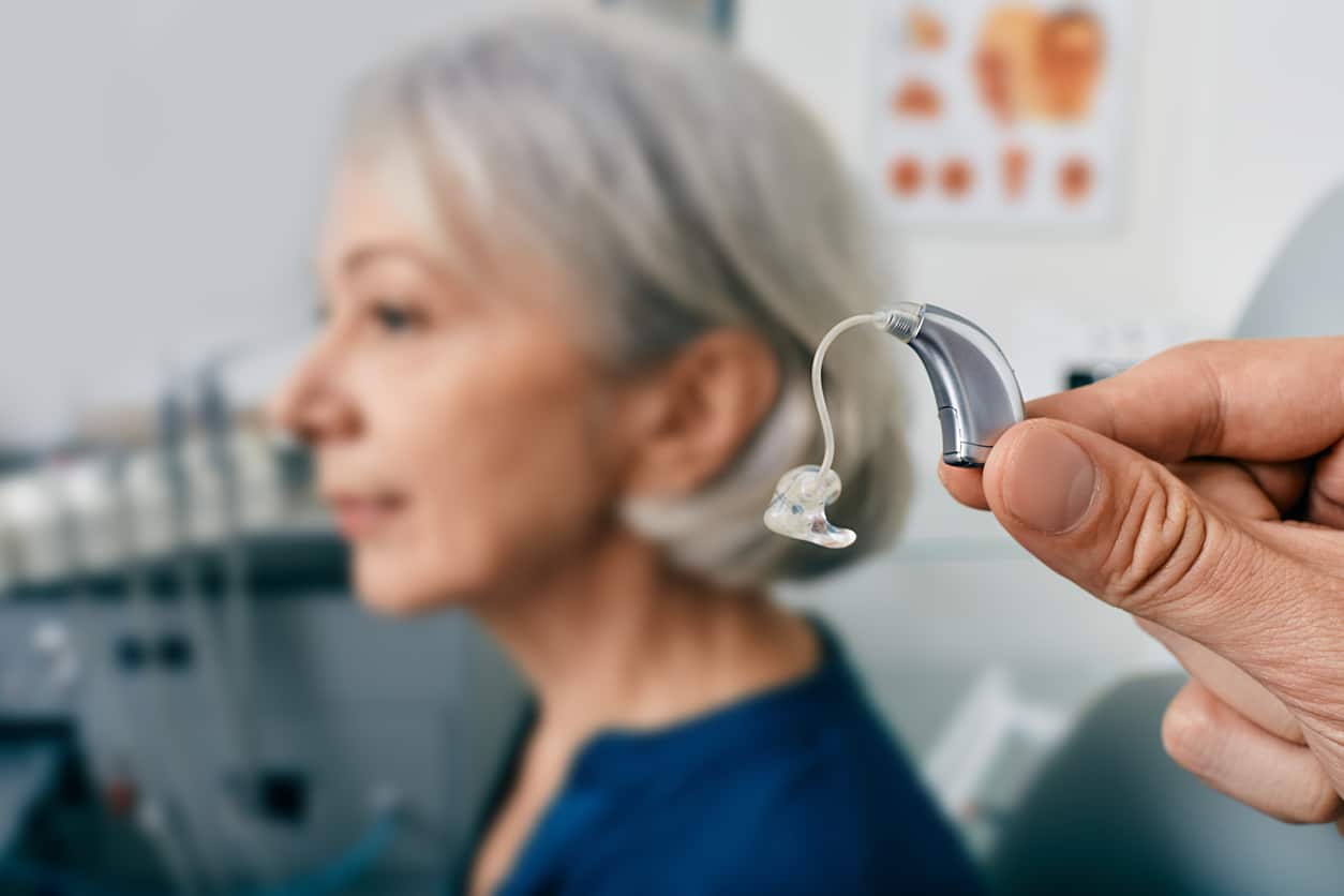 Close up of a hearing aid near a senior patient's ear.