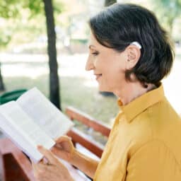 Senior woman with hearing aids reading a book in a local park.