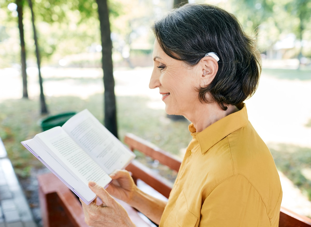 Senior woman with hearing aids reading a book in a local park.